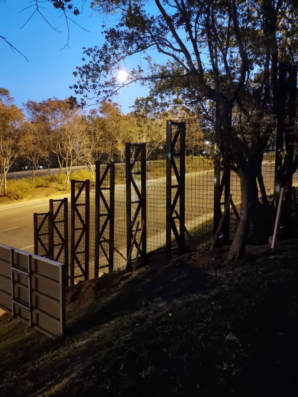 High-Security Double Wire Mesh Fencing with Intermediate Anti-Climb Spikes Protecting the Main Road on Sloping Terrain